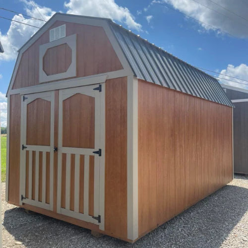 A brown wooden storage shed with a white trim and dark roof stands on gravel under a partly cloudy sky, creating a rustic and serene atmosphere.