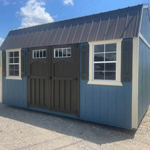 A blue and brown shed under a sunny sky, featuring double doors and two windows with white trim. The scene conveys a rustic and peaceful tone.